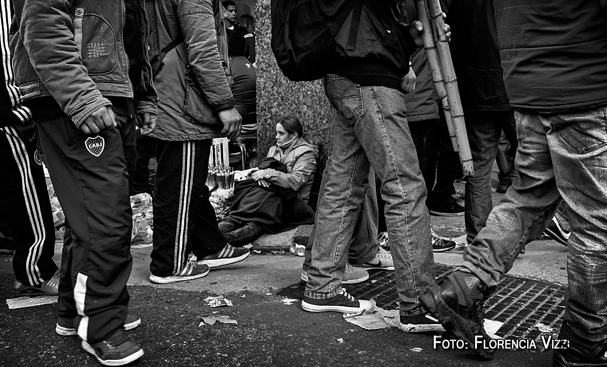 La vendedora ambulante acuna al niño y lo protege del frío. En medio de la protesta nadie parece reparar en ella…