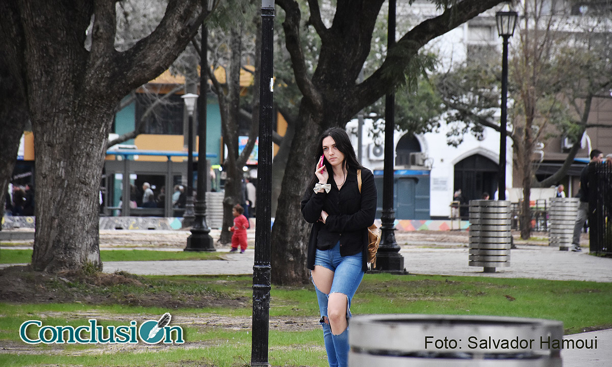 Pendiente del celular y a la moda, caminando por Plaza Sarmiento